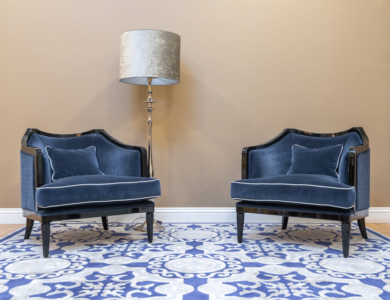 Pair of luxurious blue velvet chairs and a decorative lamp against a neutral wall.